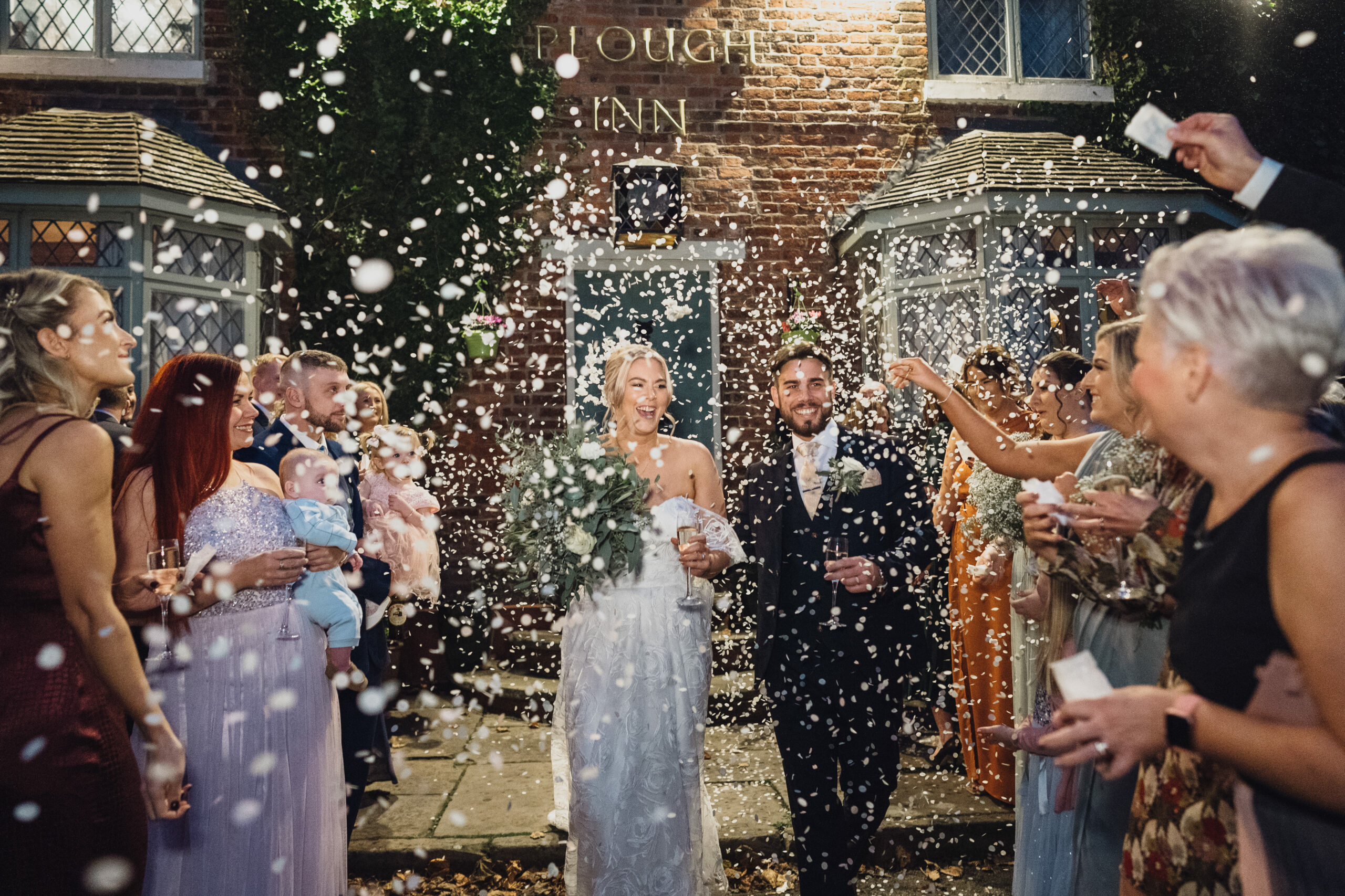 Guests throwing confetti over a bride and groom outside The Plough Inn